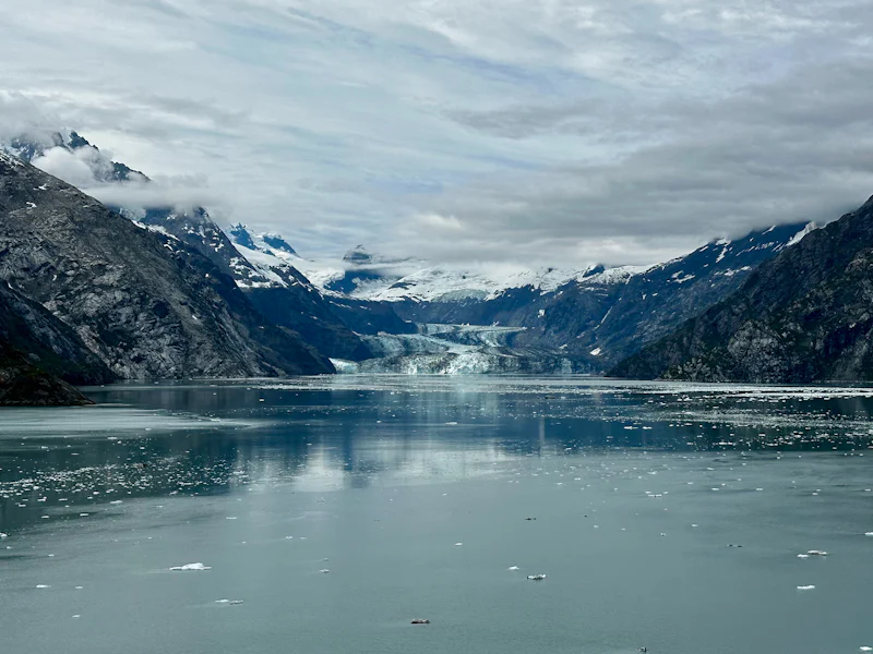 A glacier meeting a calm fjord below snow-covered mountains in Alaska
