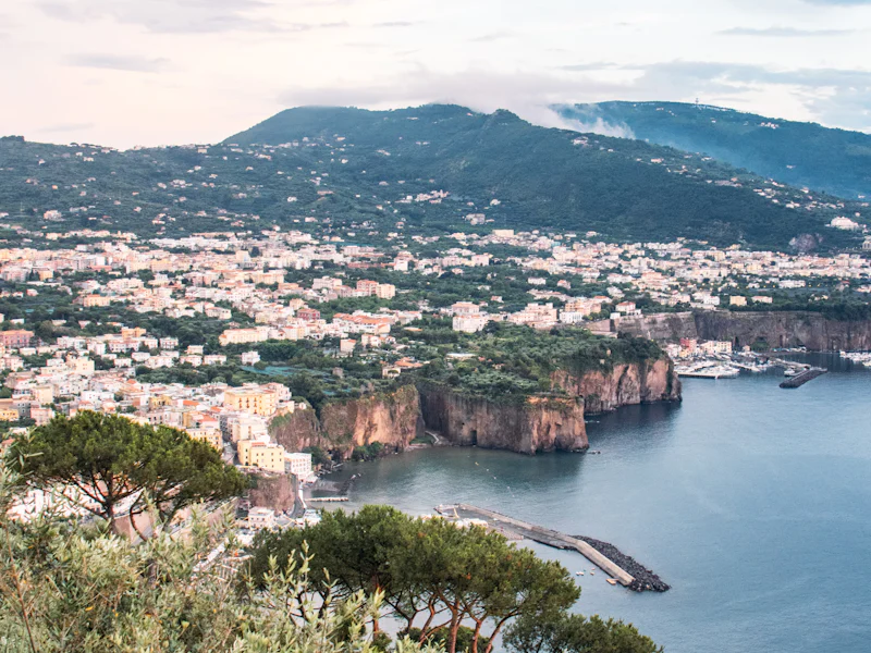 A Mediterranean coastal town on cliffs above a blue bay at dusk