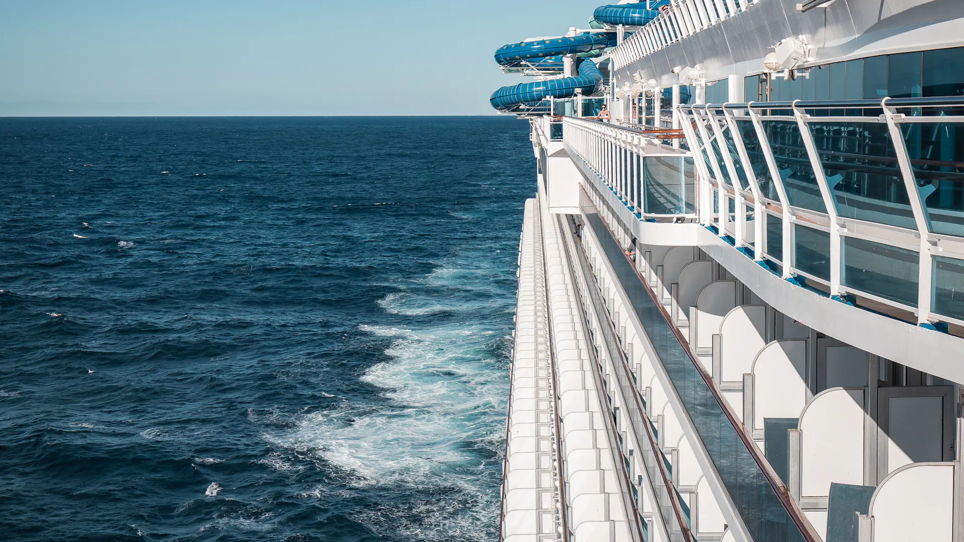 The upper decks of a cruise ship under way, with open ocean and the ship's wake alongside